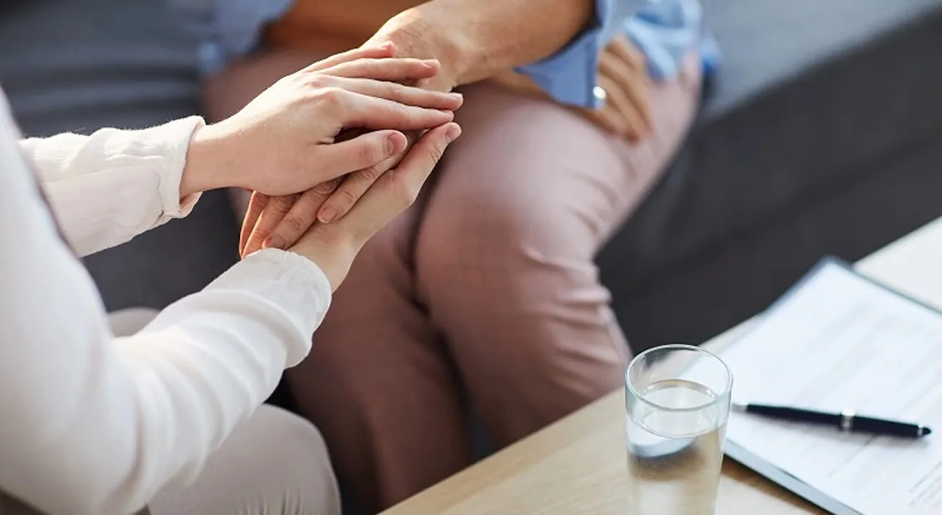 One person gently holding another person’s hands during a supportive conversation