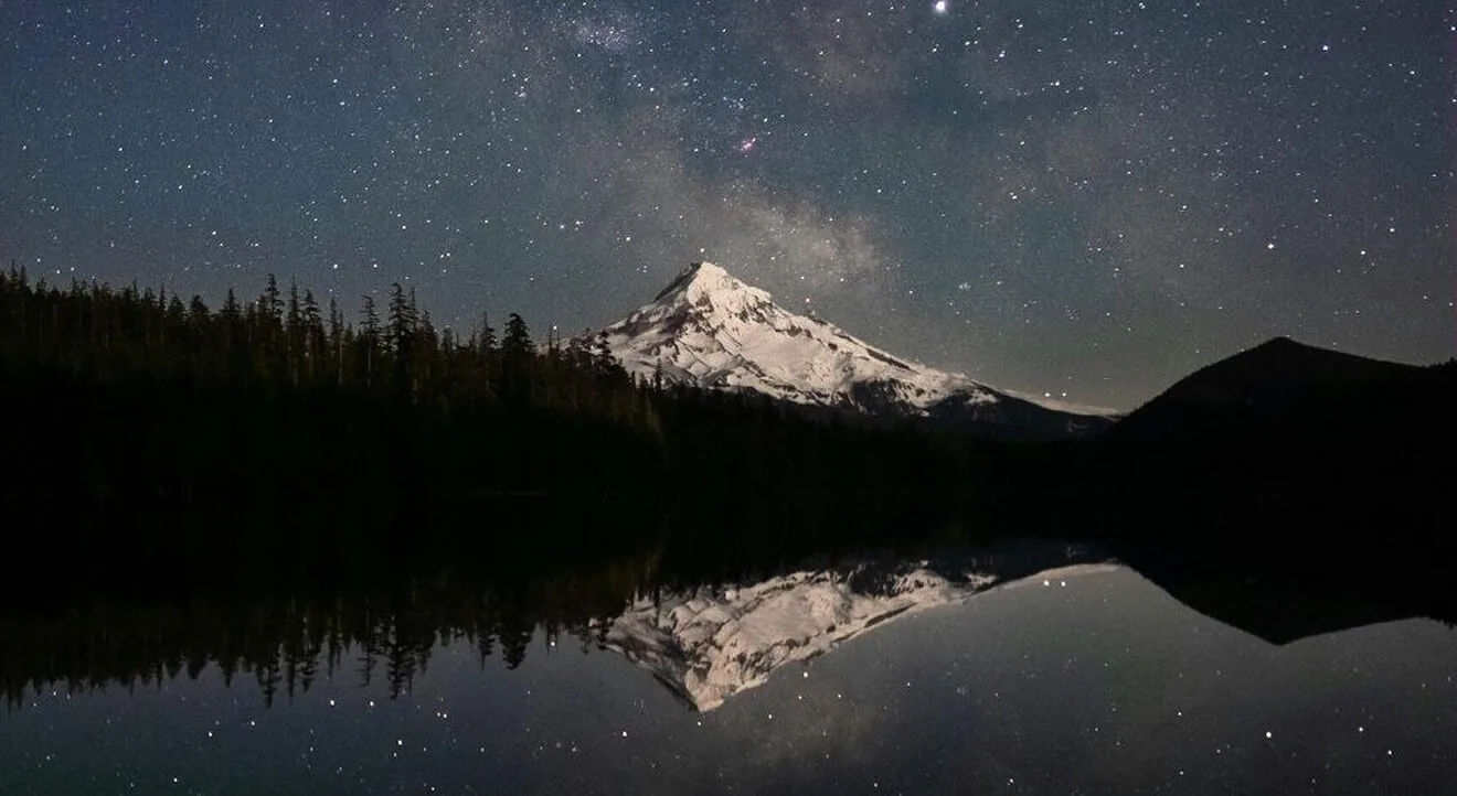 Star-filled night sky above a snow-covered mountain reflected in a lake
